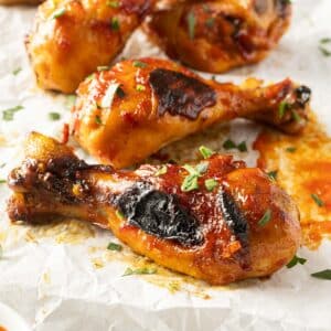 Close-up of honey harissa-glazed chicken drumsticks with herb garnish on a piece of parchment paper.
