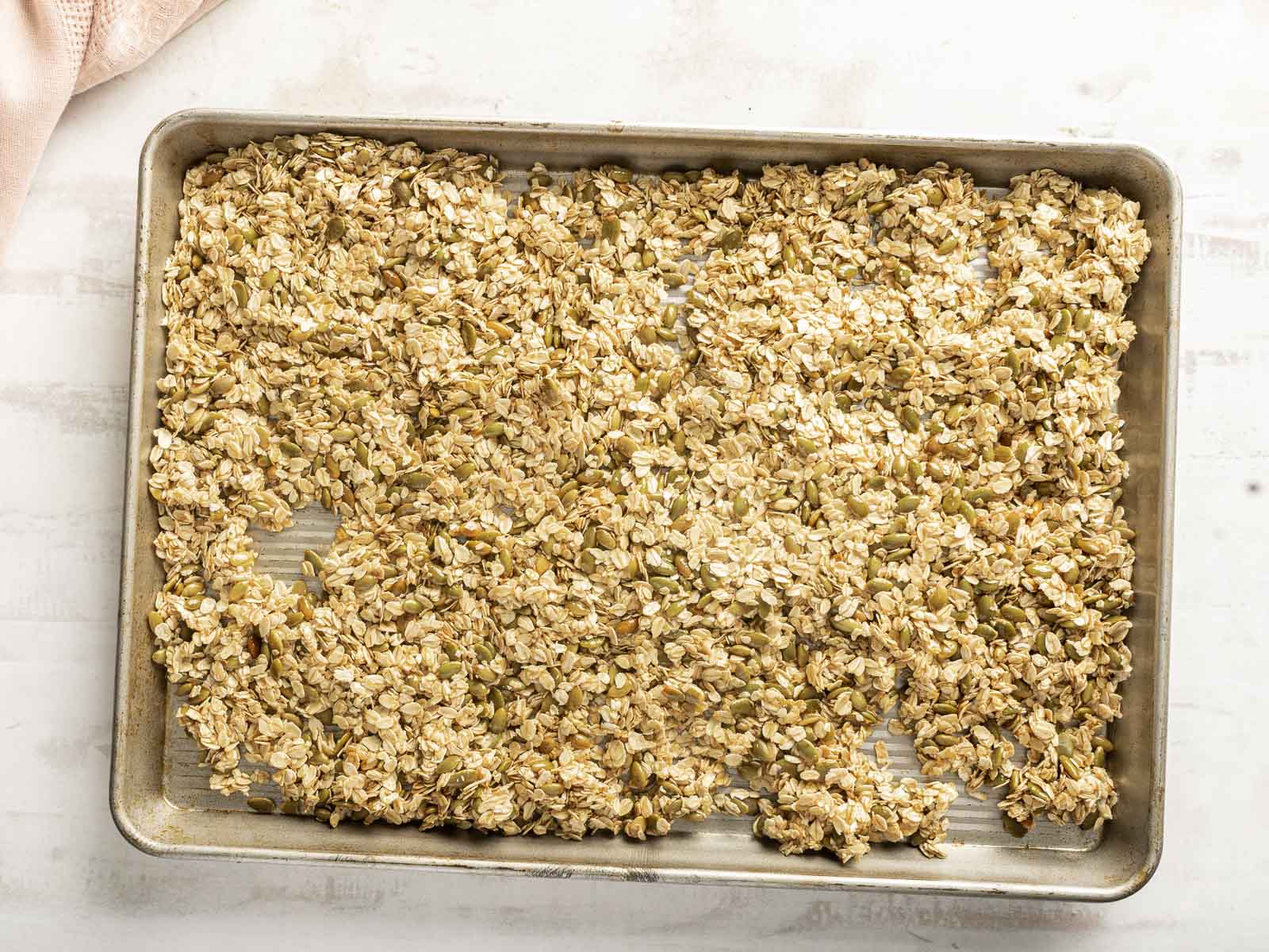 A baking tray filled with a mixture of uncooked granola spread evenly over parchment paper.