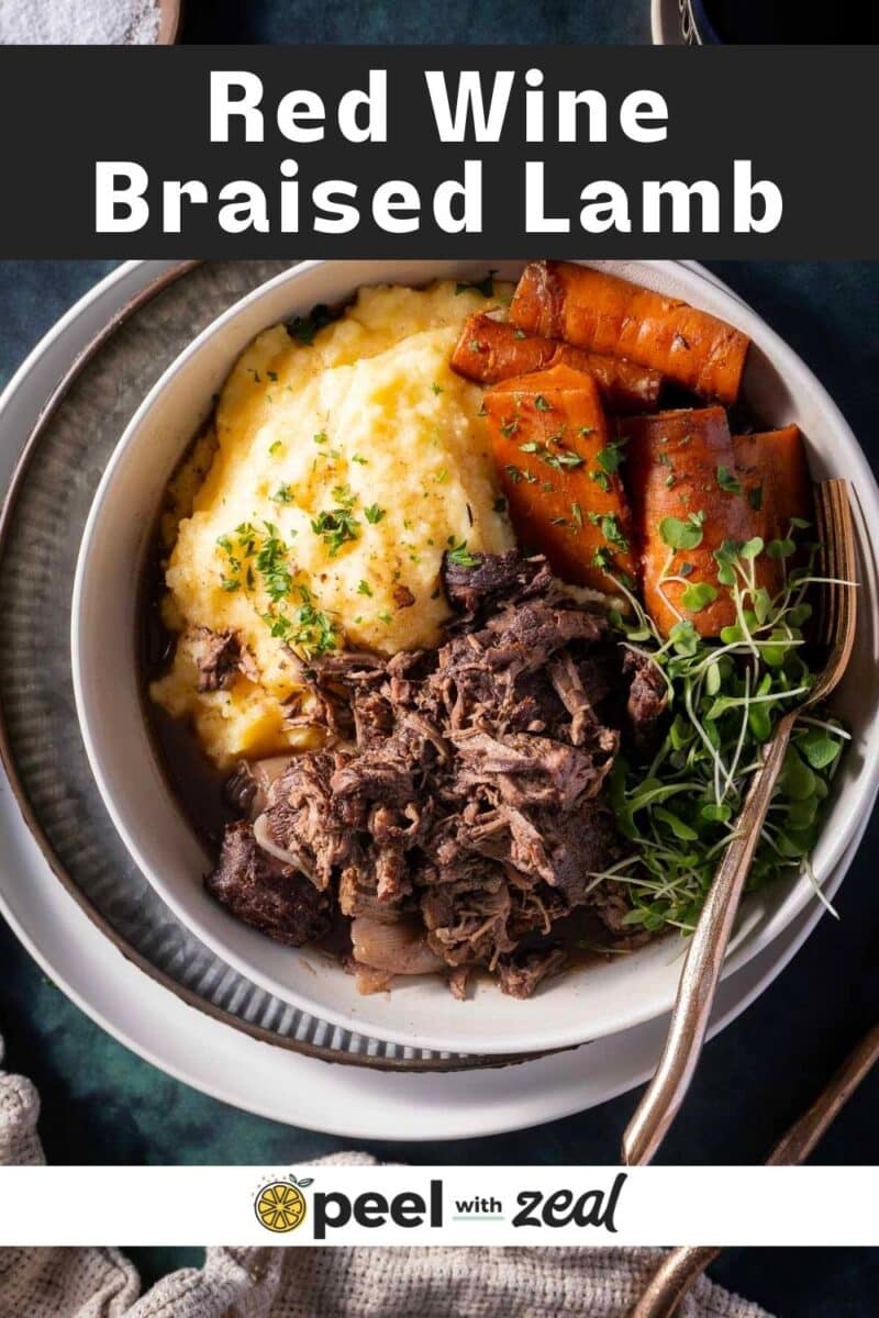 A bowl of red wine braised lamb with mashed potatoes, carrots, and garnished with herbs.