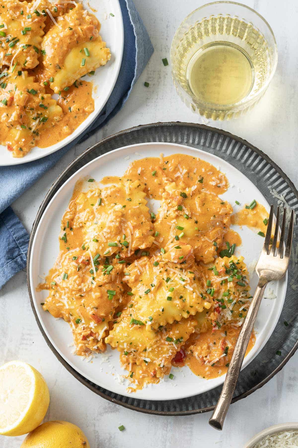 A plate of lobster ravioli topped with creamy sauce and herbs, served with a fork. A glass of white wine is beside the plate.