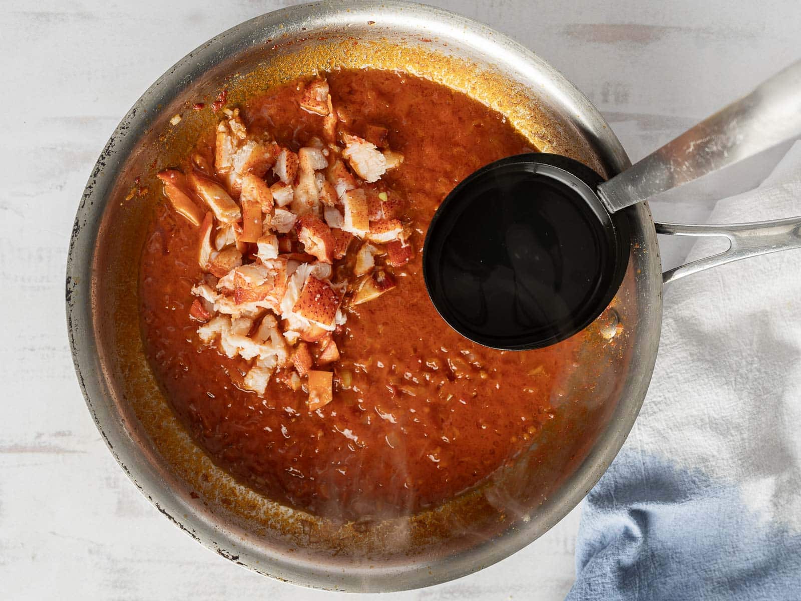 A pan filled with rich tomato soup and pieces of chopped cooked fish, with a ladle resting on the edge, evokes the comforting essence of a creamy lobster ravioli.