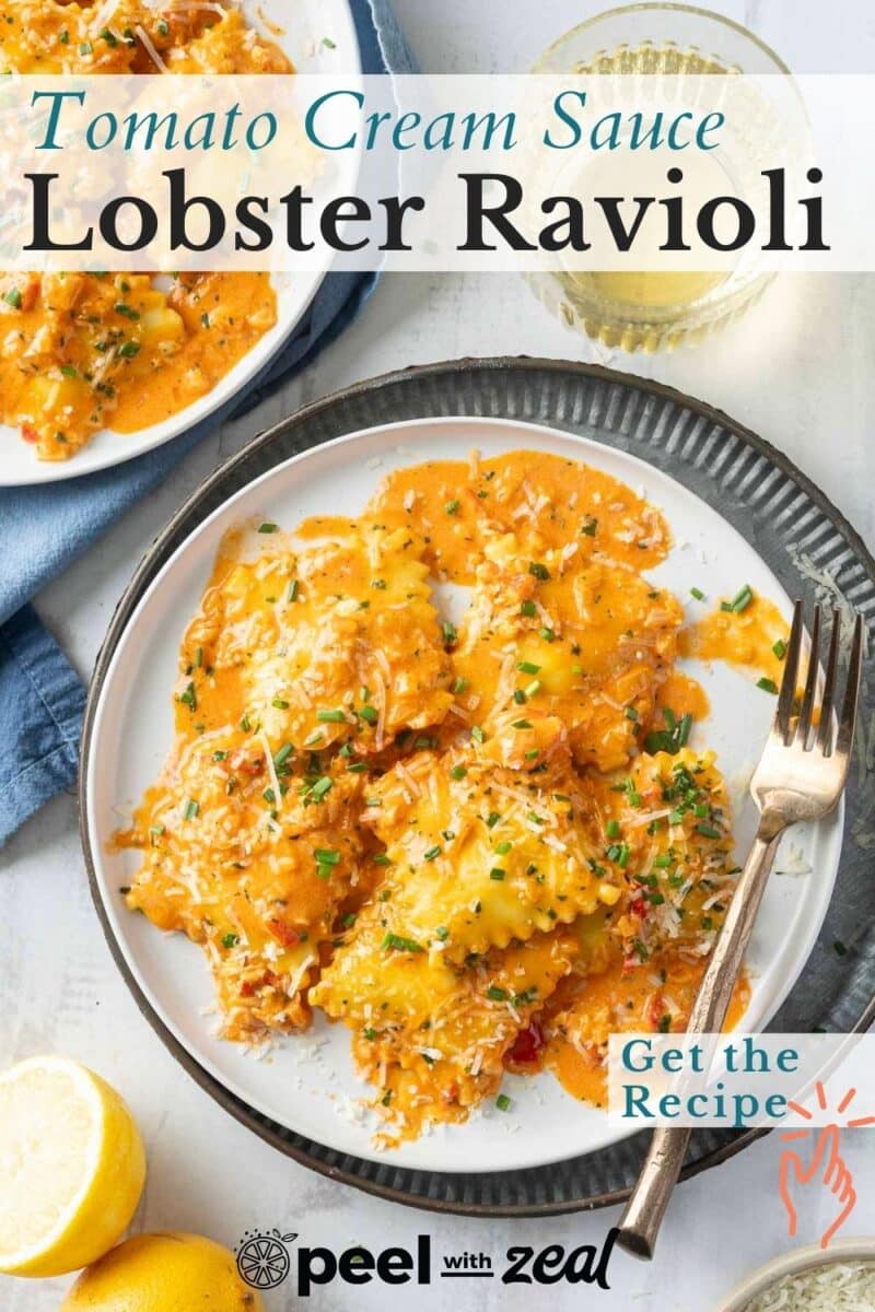 Plate of lobster ravioli topped with tomato cream sauce, garnished with herbs and cheese, next to lemons and a glass of white wine.