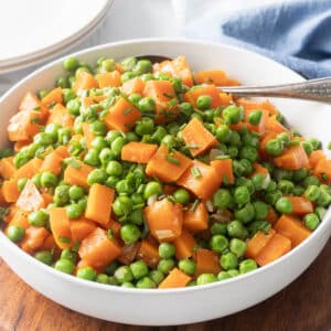A bowl of peas and carrots, perfectly mixed and garnished with fragrant chopped herbs.