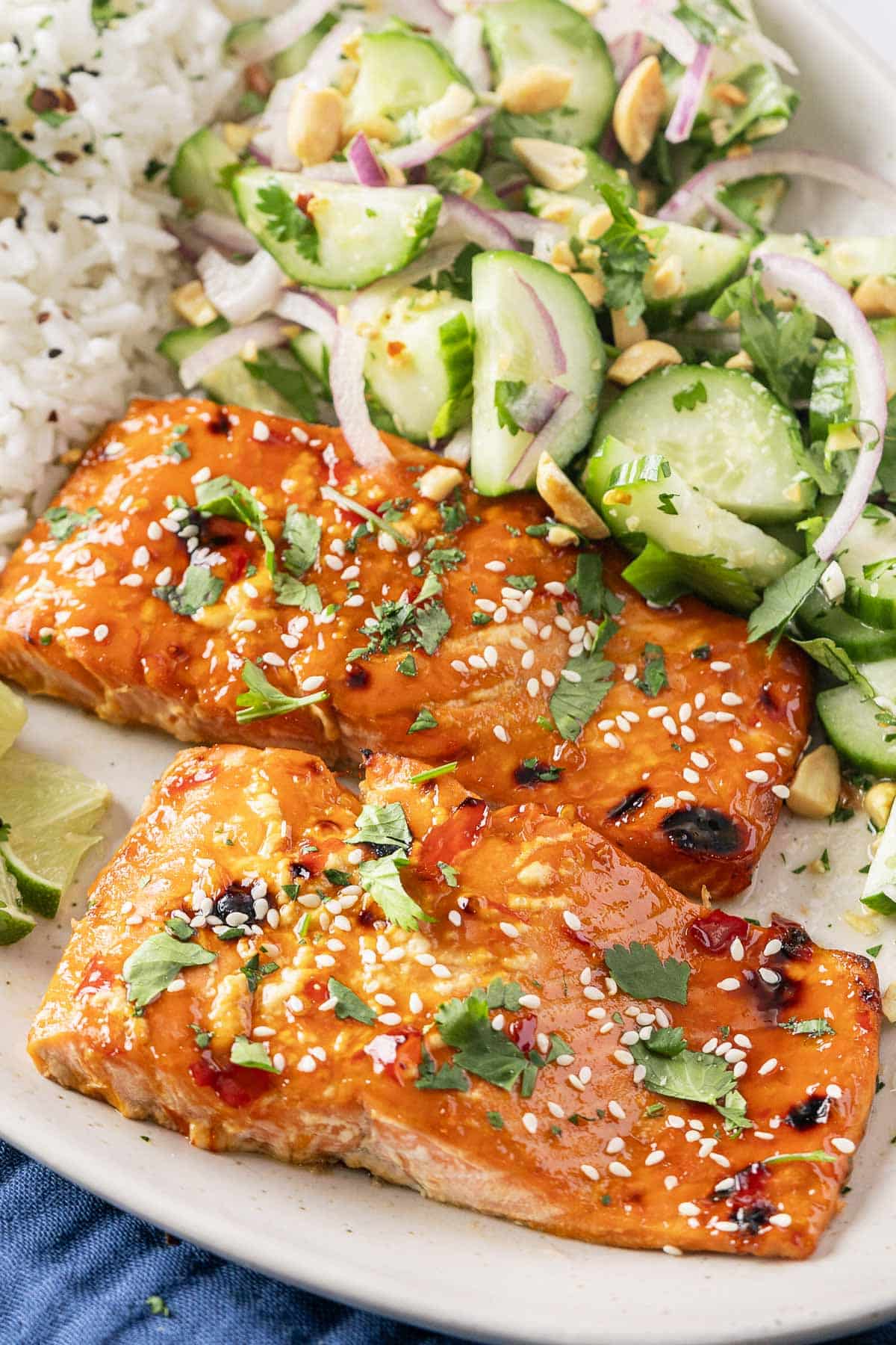 Sweet Chili Salmon, grilled to perfection and topped with sesame seeds and herbs. It comes with a refreshing cucumber salad and fluffy jasmine rice, all beautifully garnished with lime wedges for an extra zest.