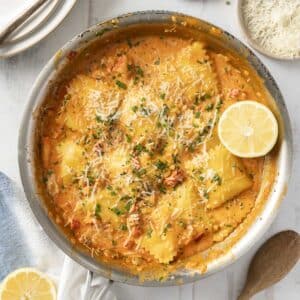 A skillet of lobster ravioli in a creamy tomato sauce, topped with grated cheese and herbs, and garnished with a lemon slice.
