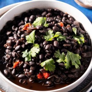 A bowl of slow-cooked black beans garnished with fresh cilantro and small red chili pieces.