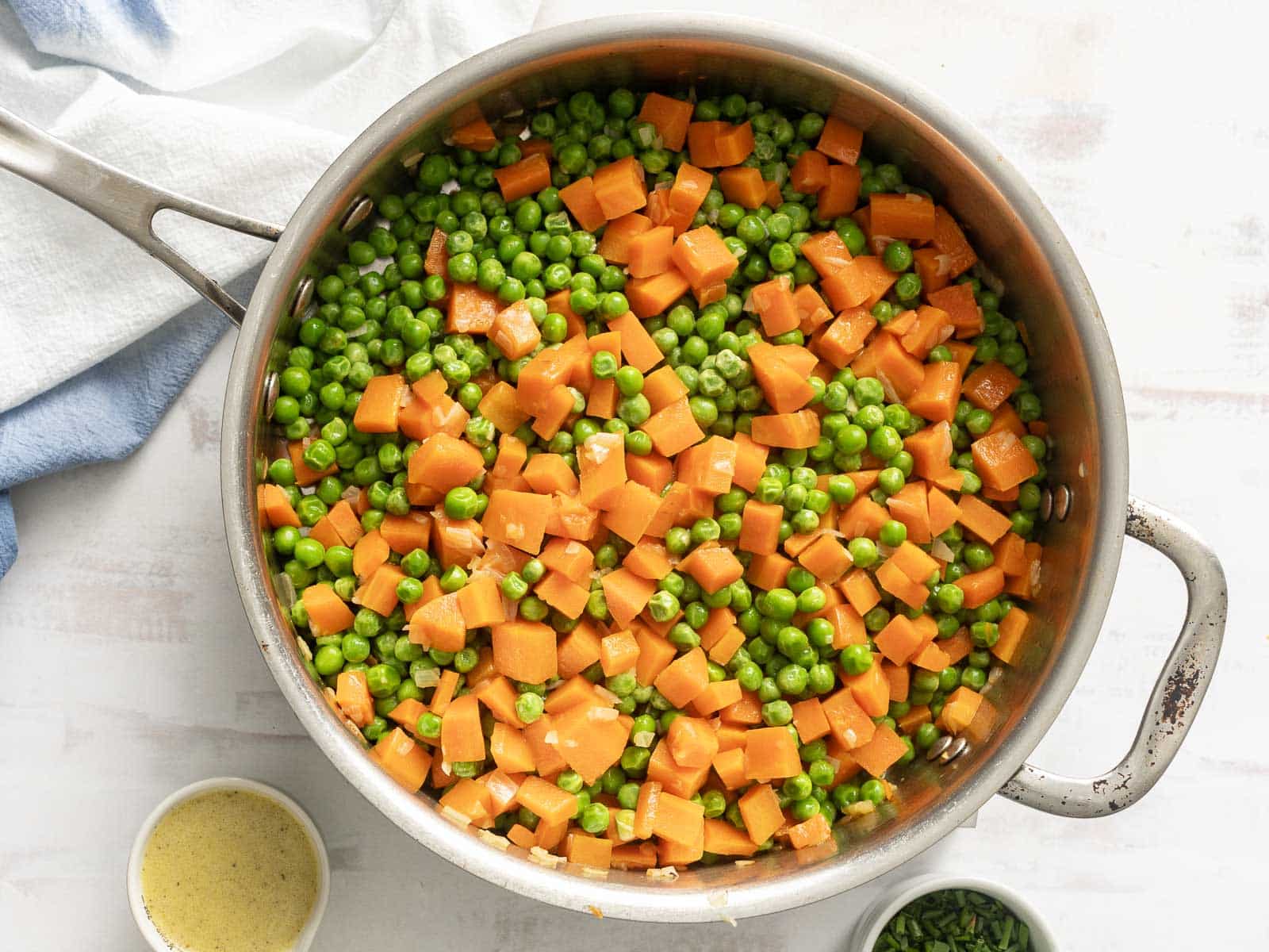 A stainless steel pan brimming with a harmonious medley of cooked peas and carrots.