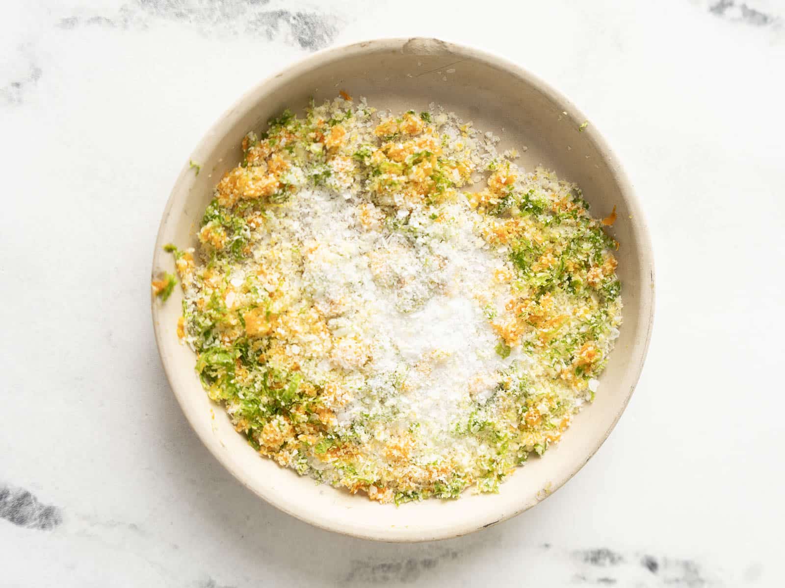A bowl filled with grated citrus zest and coarse salt sits on a white marble surface, perfect for rimming your next Margarita.