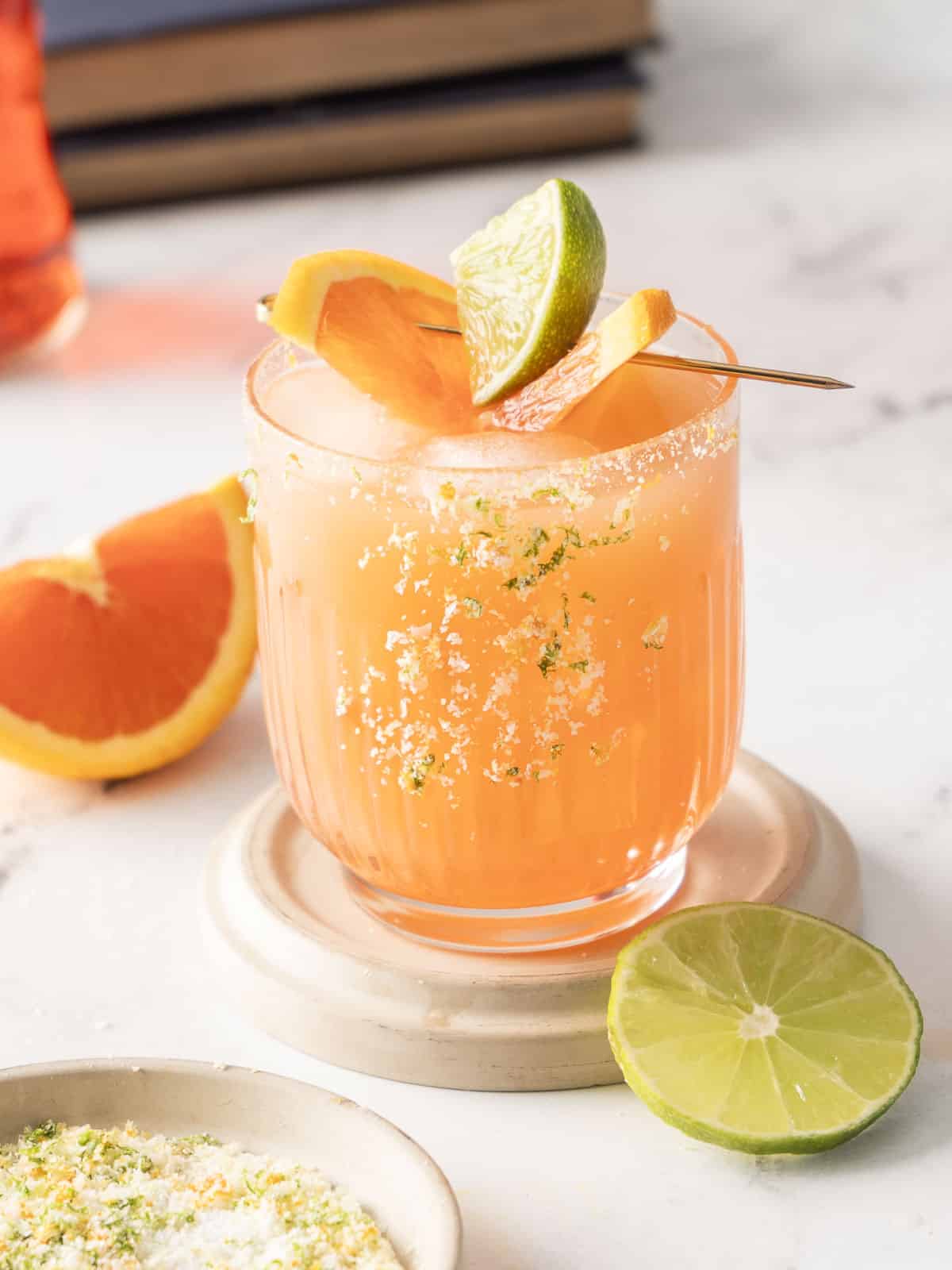 A vibrant Aperol Margarita graces a marble surface, its salted rim adding flair. Garnished elegantly with orange and lime slices, this bold twist on a classic cocktail shines in vivid hues of orange.