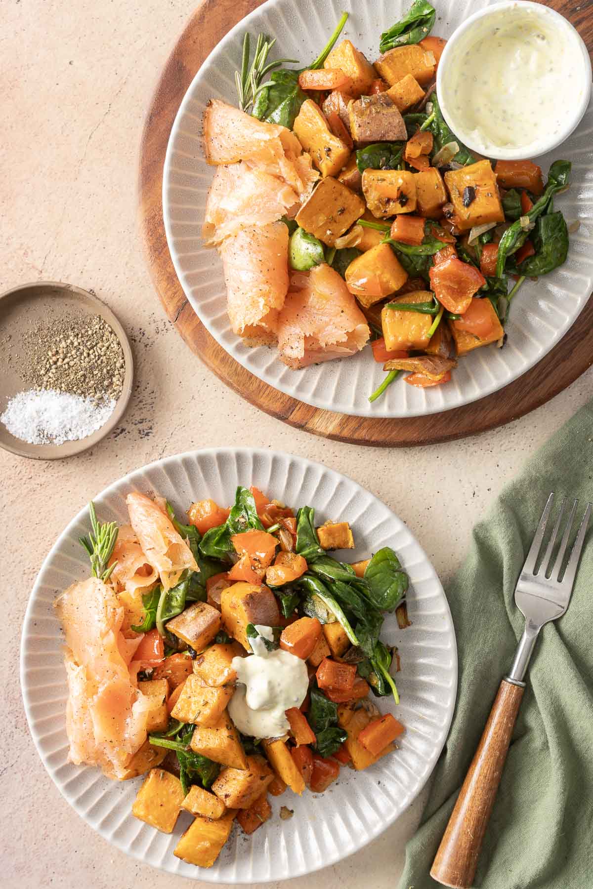 Two plates with smoked salmon, roasted sweet potatoes, spinach, and a small bowl of creamy dressing on one plate.