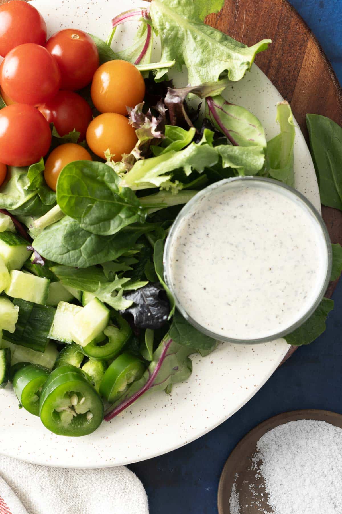 A plate of salad with cherry tomatoes, greens, cucumbers, jalapeños, and a bowl of garam masala-infused ranch dressing on the side.