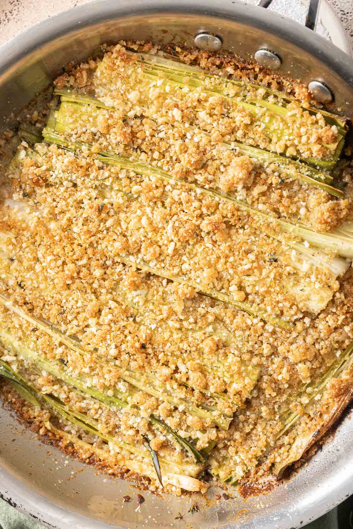 A dish of roasted leeks topped with a golden breadcrumb crust in a metal pan.