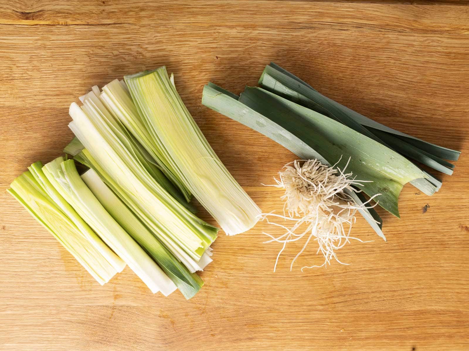 Leeks cut in half and trimmed on a cutting board. 