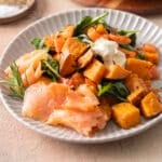 A plate with smoked salmon, roasted sweet potatoes, spinach, and a dollop of sauce.