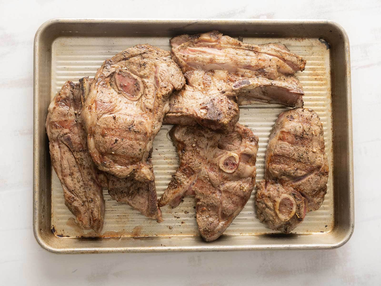 Grilled lamb shoulder chops rest on a metal tray.