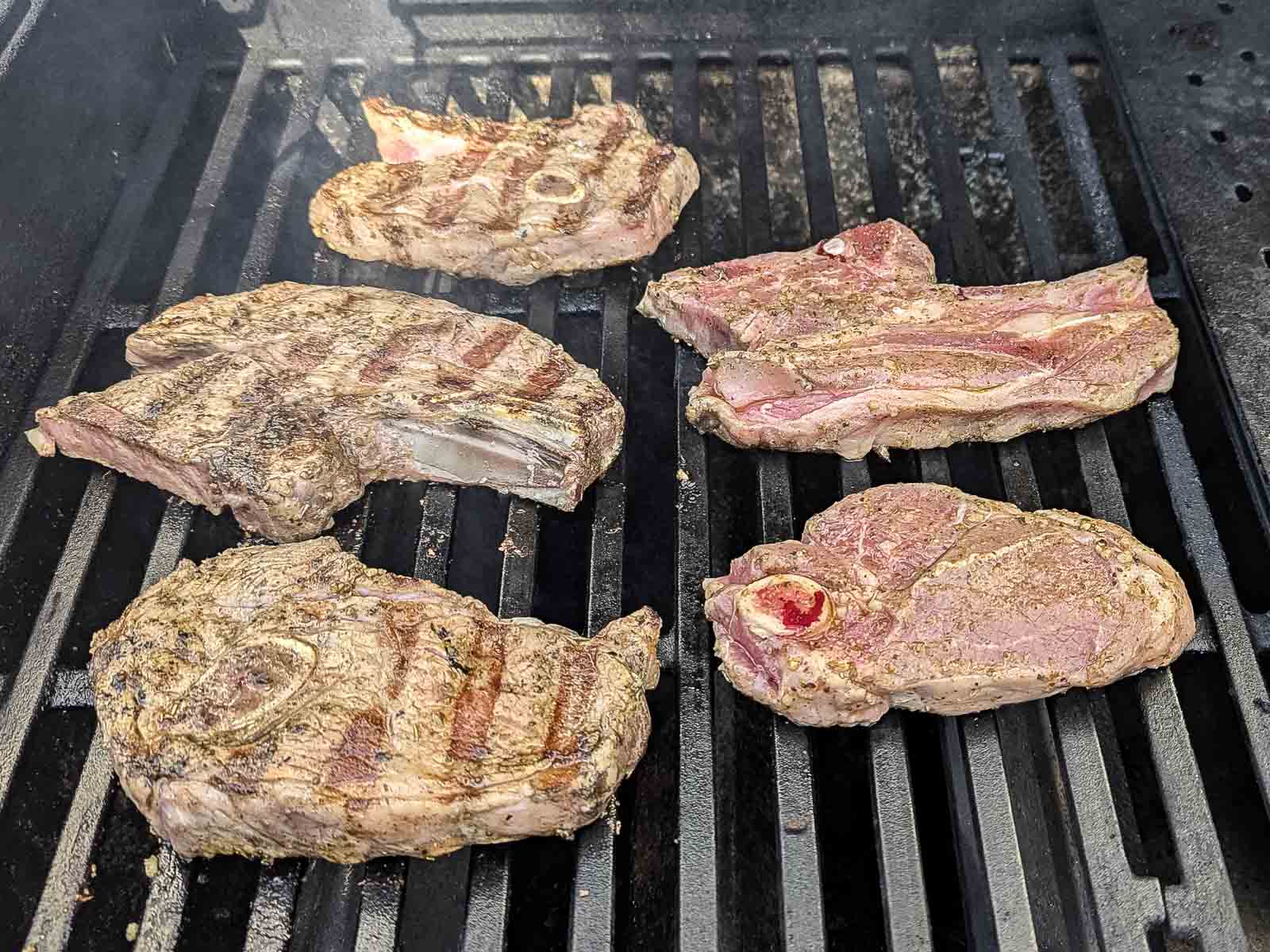 Five seasoned lamb shoulder chops sizzle on the barbecue, each marked with perfect grill lines.