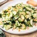 A delightful zucchini salad graces a round white plate, artfully adorned with pine nuts and fresh herbs.