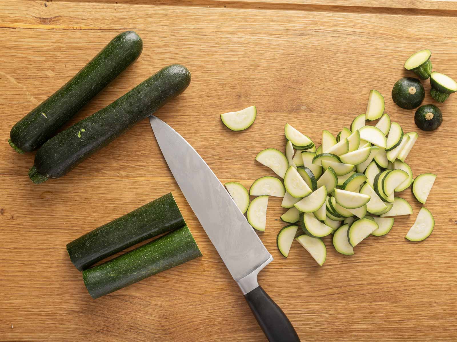 Sliced zucchinis for a refreshing zucchini salad, paired with a knife on a wooden cutting board.