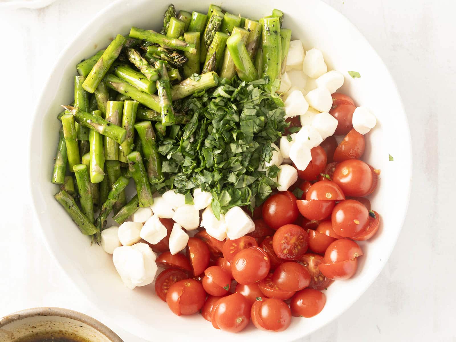 White bowl with grilled asparagus, mozzarella, cherry tomatoes, and fresh basil, arranged in separate sections.