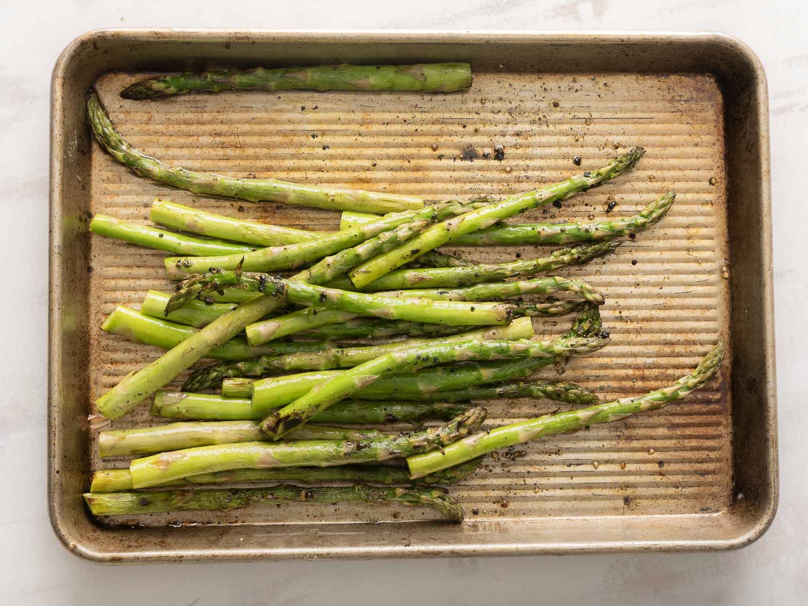asparagus spears lay on a seasoned baking sheet, ready to become the star of a vibrant tomato salad.