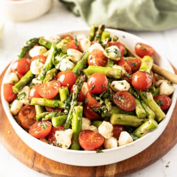 A bowl featuring a vibrant Grilled Asparagus and Tomato Salad with cherry tomatoes and mozzarella balls, elegantly arranged on a wooden board.