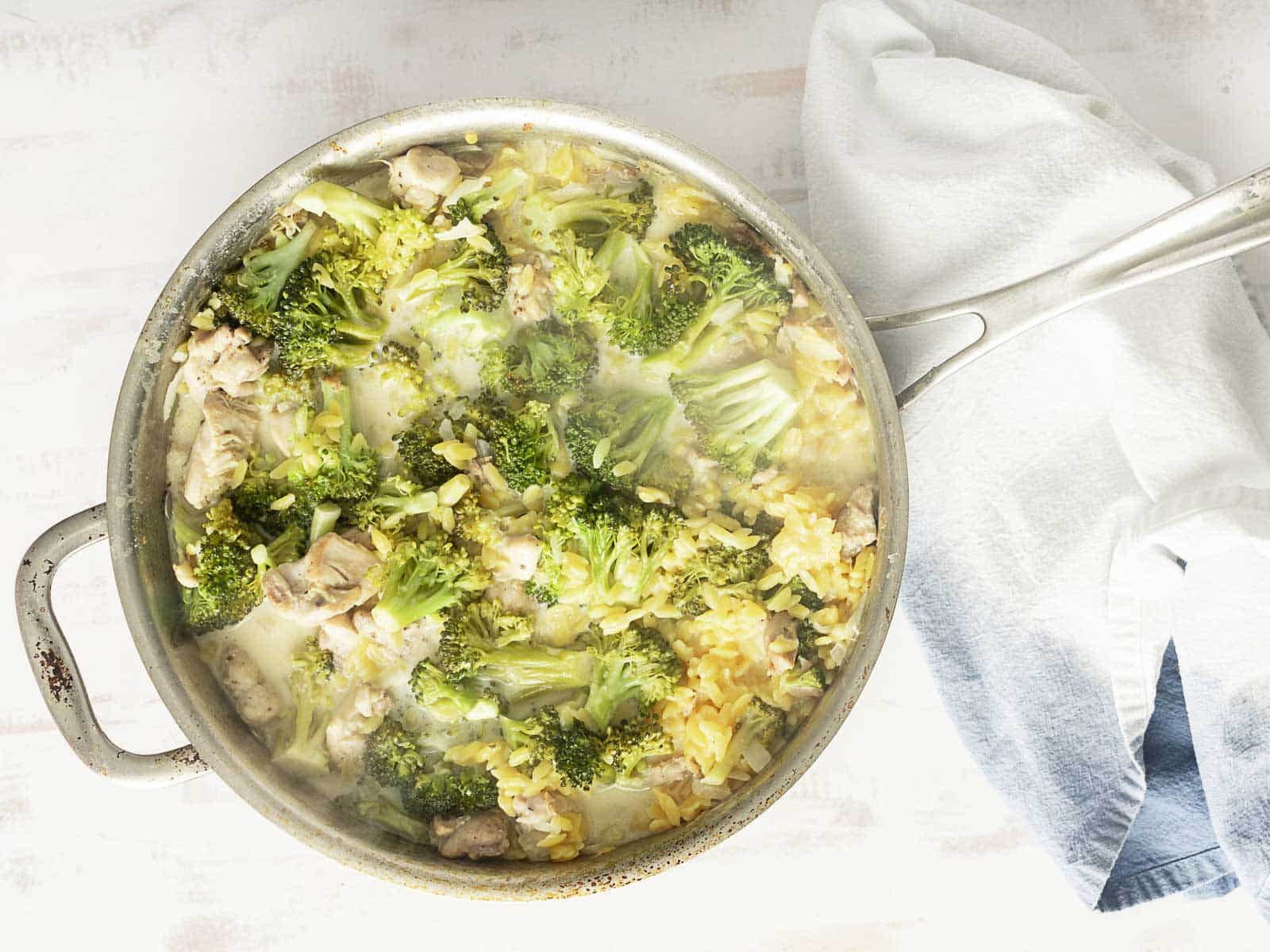 A skillet filled with broccoli, rice, and chicken sits beside a white and blue towel, offering a simple one pot recipe for a comforting meal.