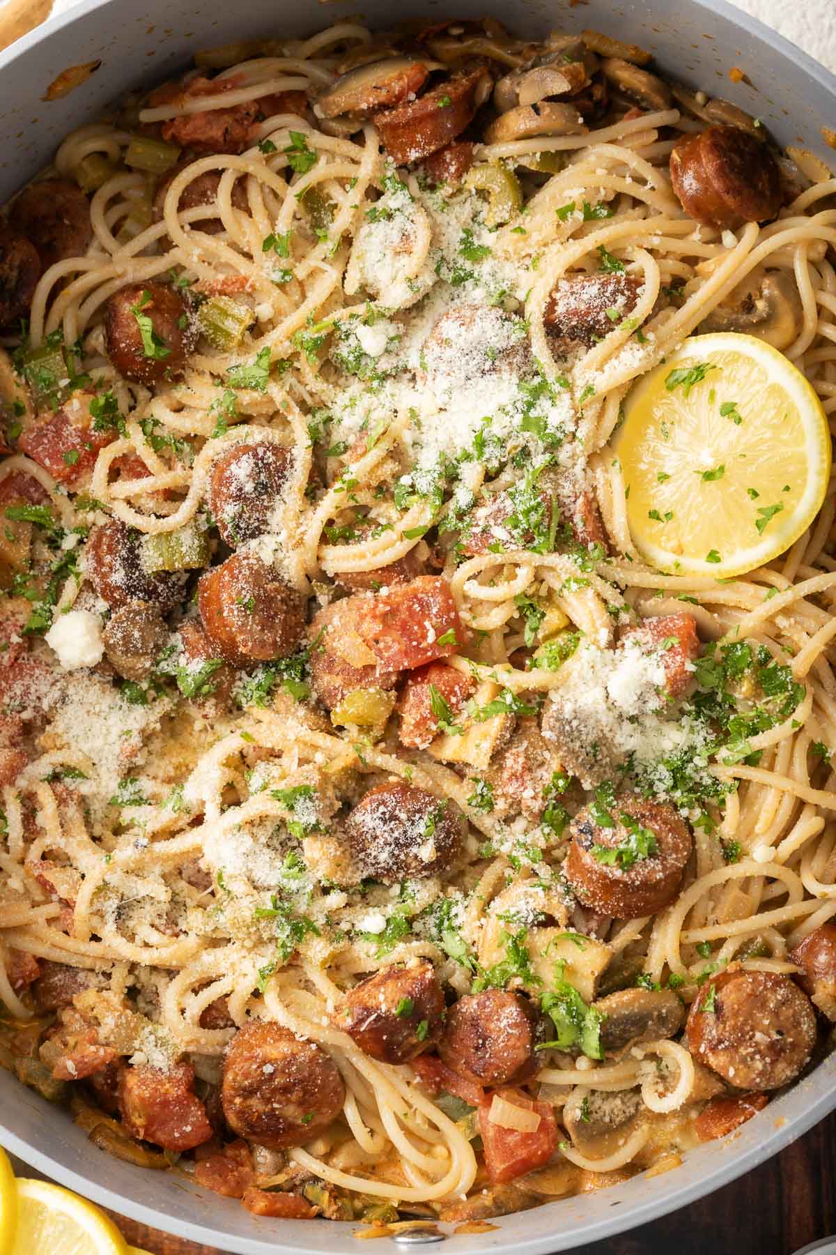 Cajun-style spaghetti with sausage, garnished with grated cheese, parsley, and lemon slices in a large pan.