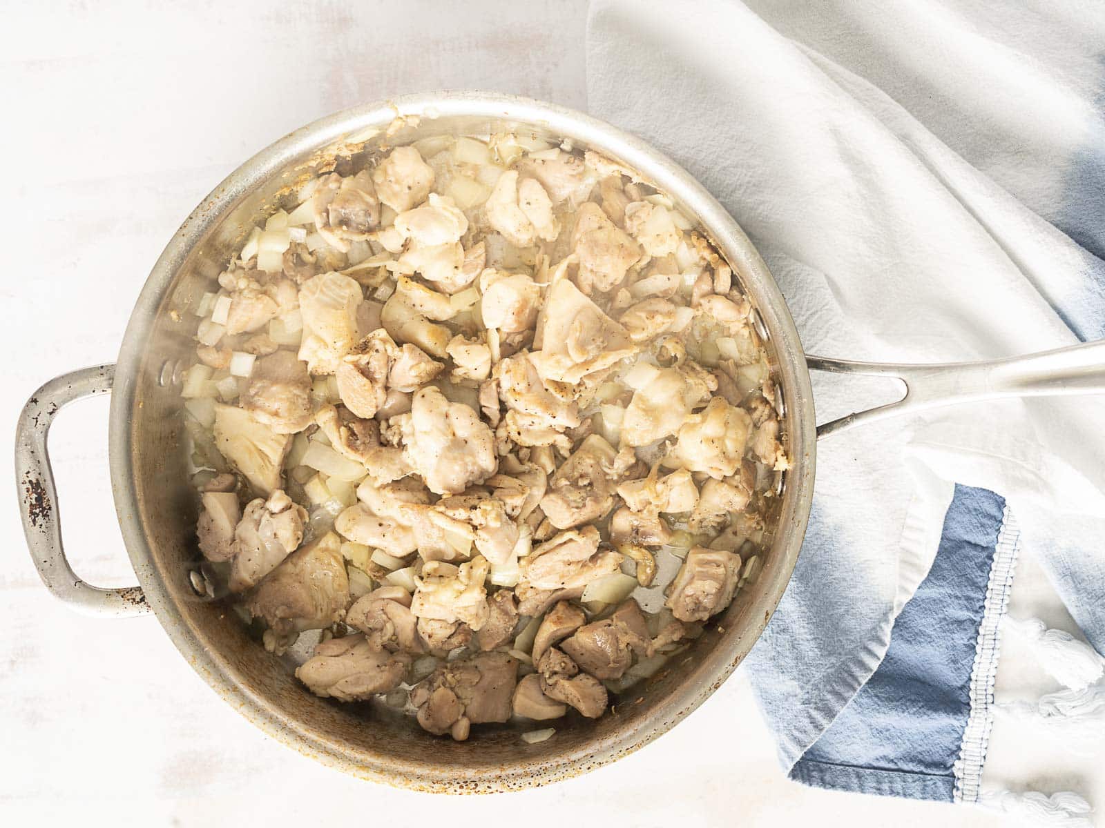 Chunks of cooked chicken and onions simmering in a pan beside a white and blue cloth, creating the perfect base for a creamy Boursin one-pot delight.