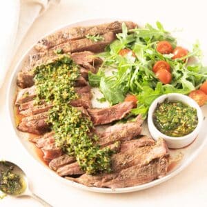 Grilled flank steak slices paired with zesty chimichurri sauce, nestled on a bed of arugula and cherry tomatoes.