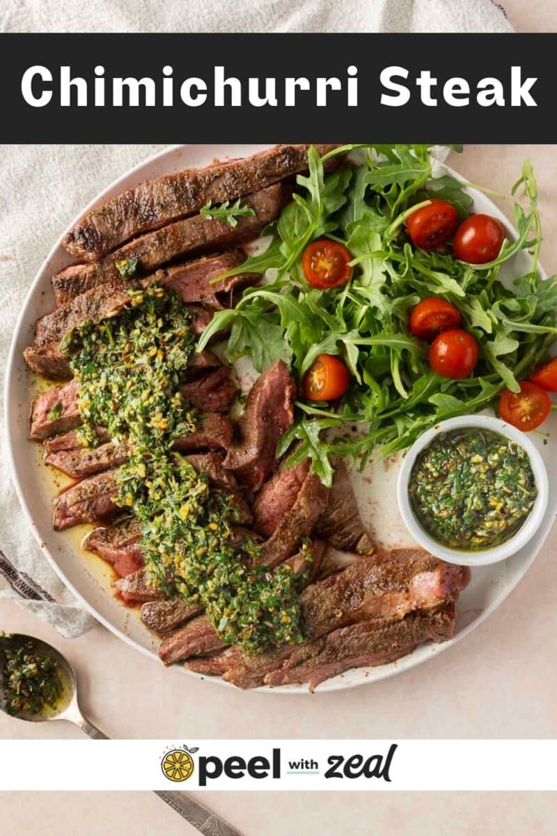 Sliced flank steak with chimichurri sauce, arugula, and cherry tomatoes artfully arranged on a plate.