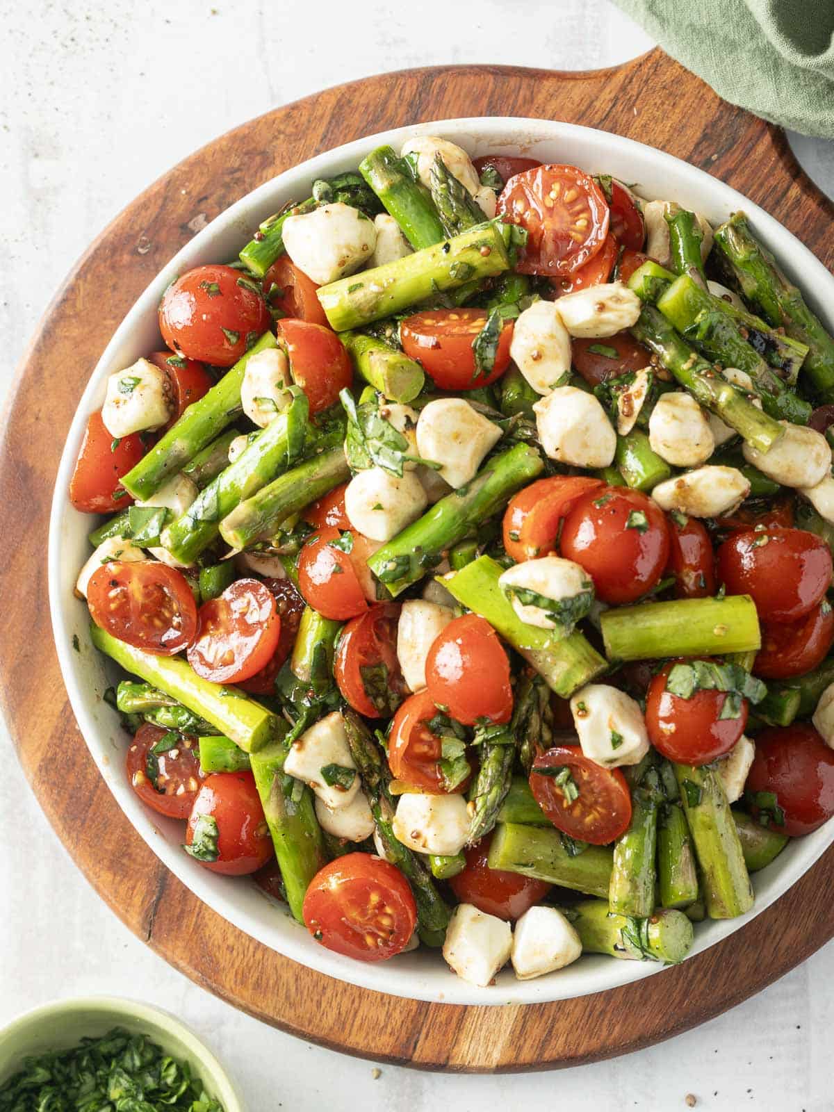 A wooden board showcases a vibrant tomato salad featuring cherry tomatoes, mozzarella, and herbs.