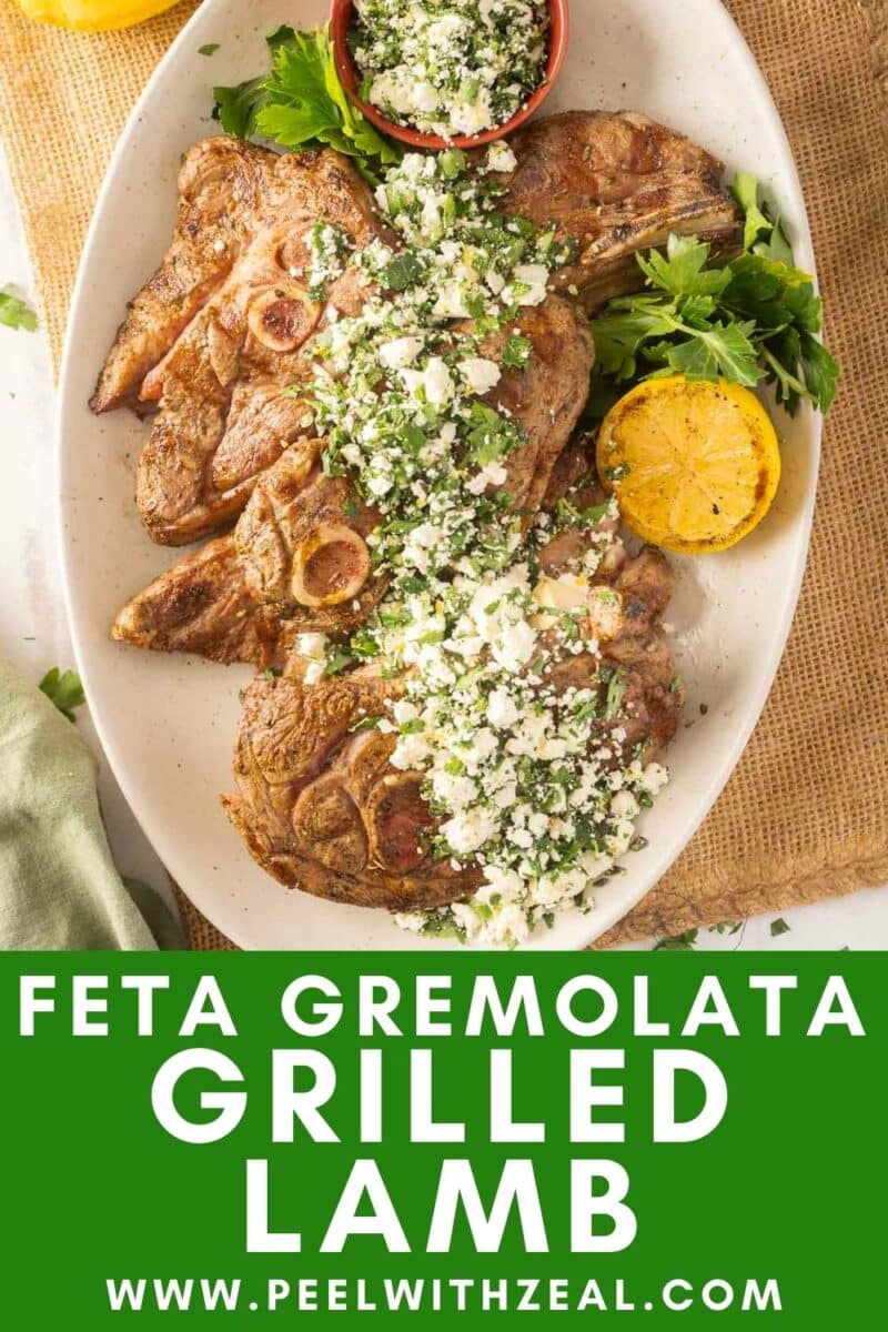Grilled lamb shoulder chops with feta gremolata, garnished with parsley and lemon, elegantly presented on a white platter.