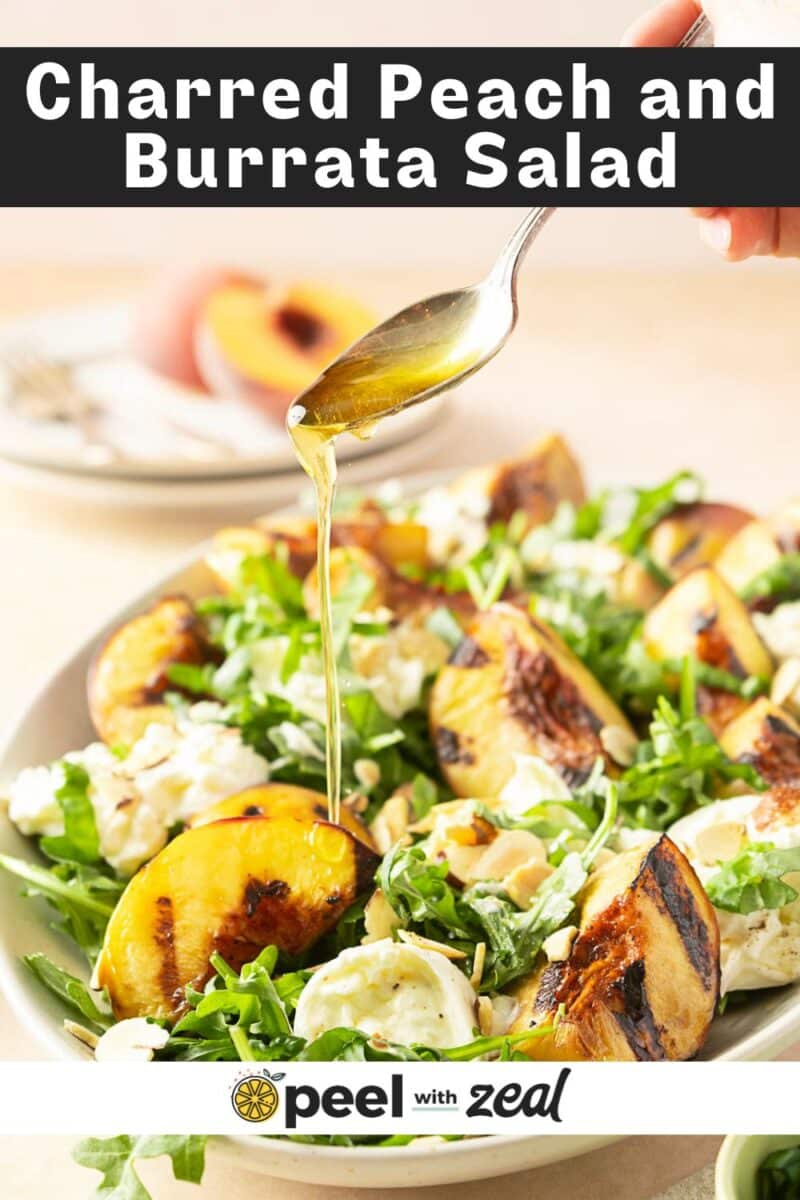A spoon drizzles dressing over a grilled peach and burrata salad, complemented by peppery arugula.
