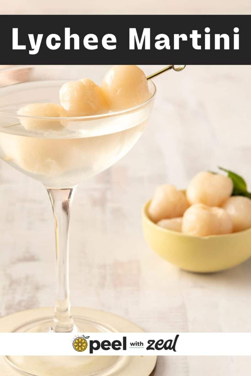 A glass of lychee martini garnished with skewered lychees sits elegantly beside a small bowl brimming with lychees.