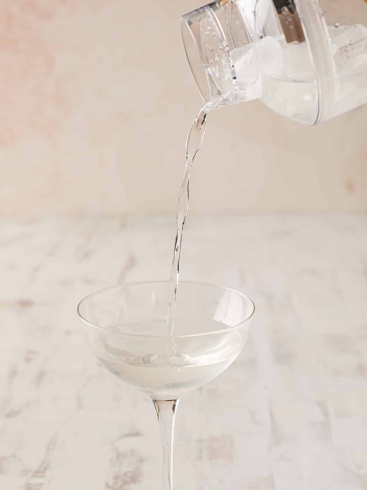 Water being poured into a clear wine glass on a light-colored surface evokes the elegance of serving a pristine martini, with its subtle allure reminiscent of the delicate essence of lychee.
