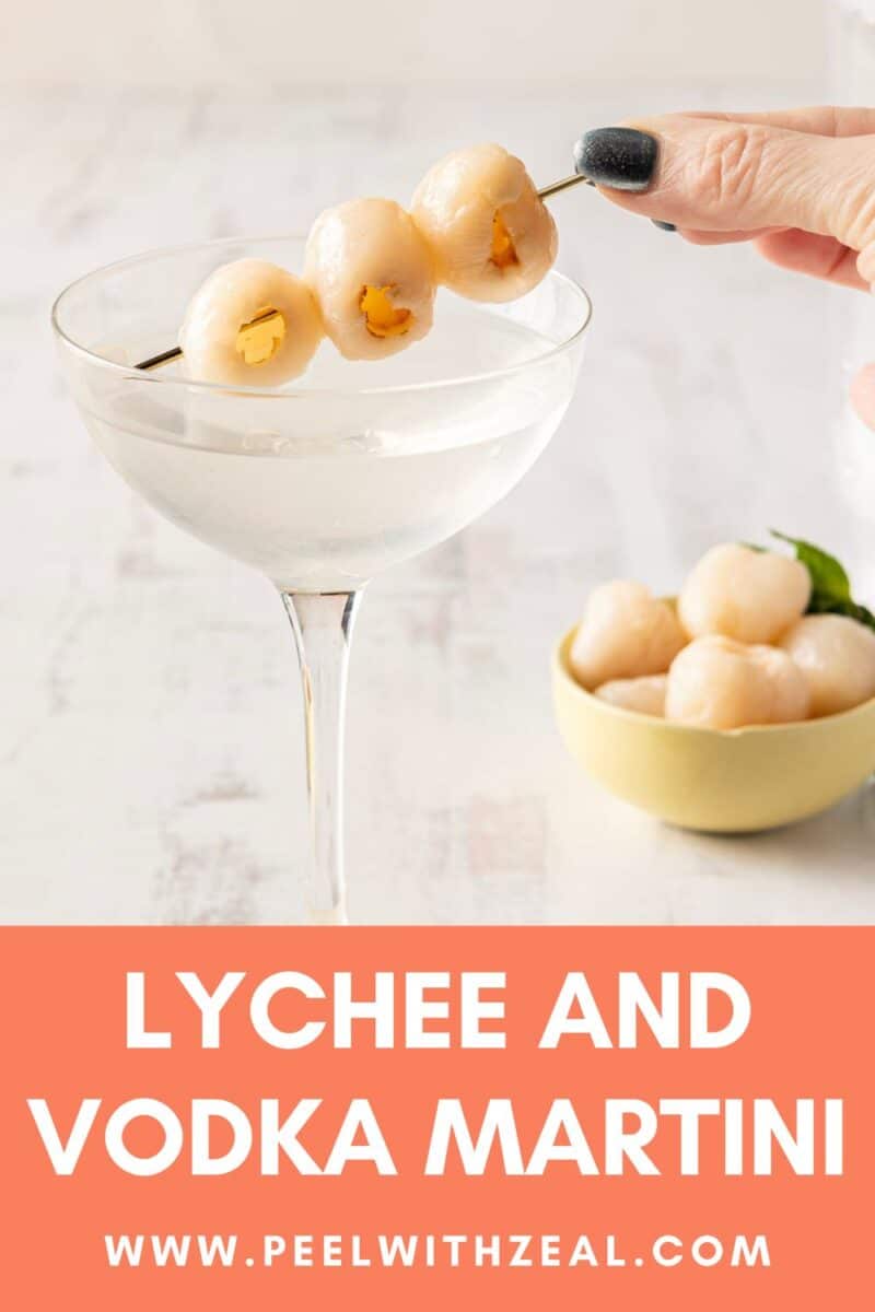 A cocktail glass with a refreshing lychee martini sits elegantly, garnished with skewered lychees. In the background, a bowl brims with more juicy lychees, inviting indulgence.