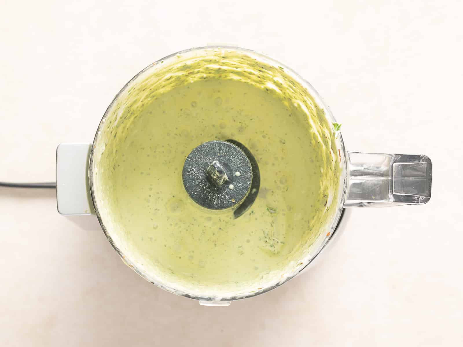 Top view of a food processor containing blended creamy chimichurri, with visible traces on the sides.