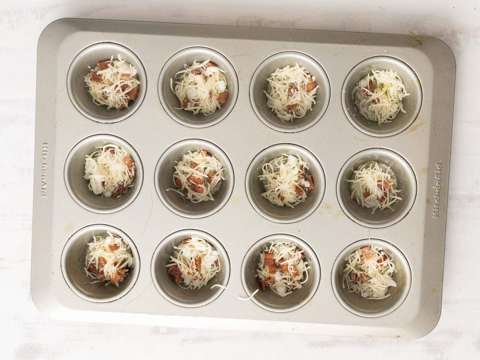 Muffin tin with 12 cups, perfect for making delicious quiche muffins, filled with shredded cheese and other ingredients, ready to bake.