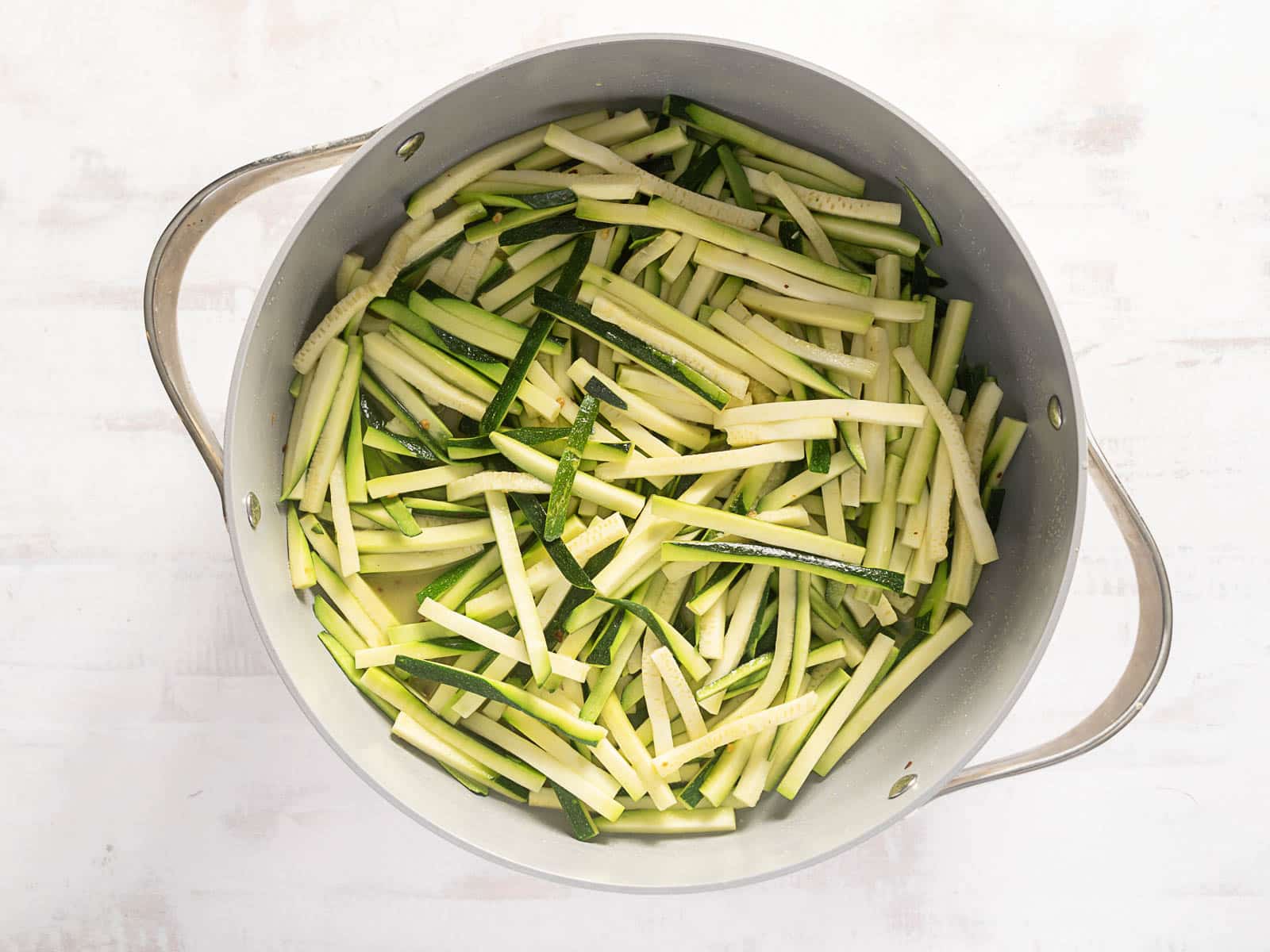 A pot filled with freshly sliced zucchini sticks, perfect for a delightful sauteed zucchini recipe, rests on a pristine white surface.