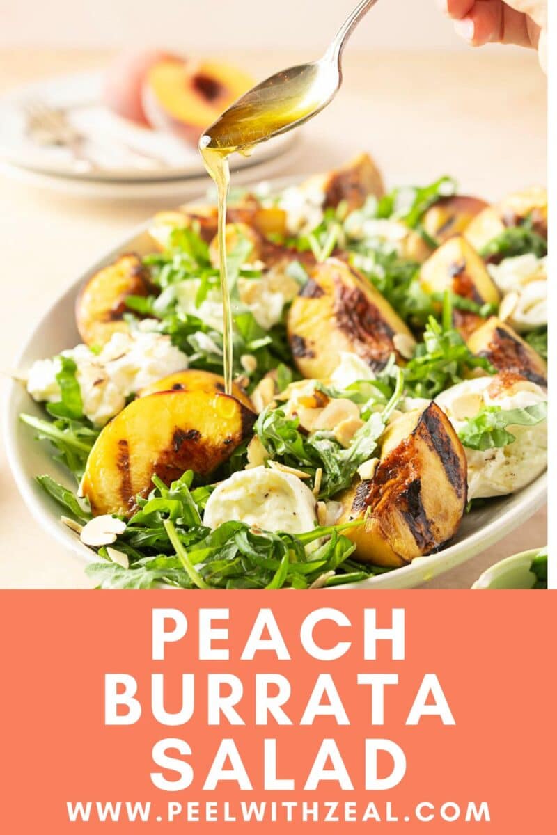 A vibrant salad featuring grilled peaches, creamy burrata, arugula, and crunchy almonds. A spoon elegantly drizzles dressing over this delightful dish.
