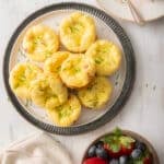 A plate of mini quiche muffins garnished with chives sits next to a bowl of strawberries and blueberries.