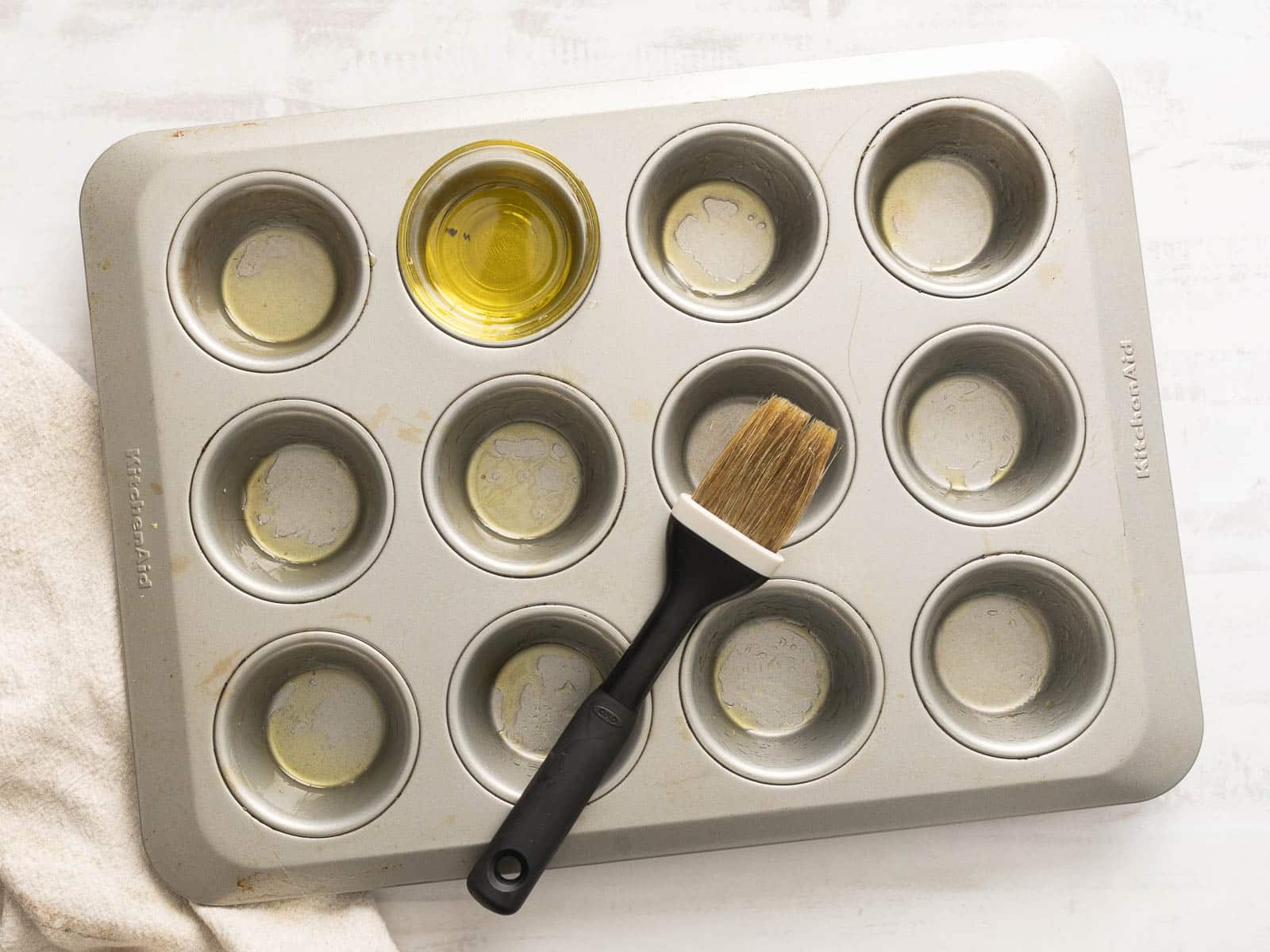 A muffin tin with butter and a brush rests on a white surface, ready for crafting delicious quiche muffins.