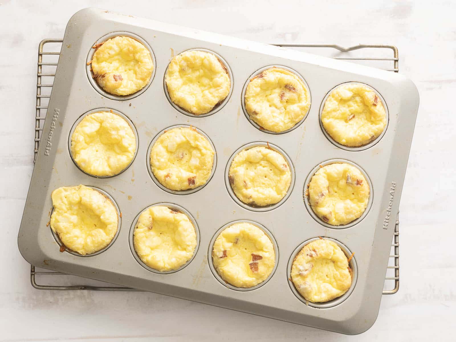 Muffin tin brimming with freshly baked quiche muffins, cooling on a wire rack.