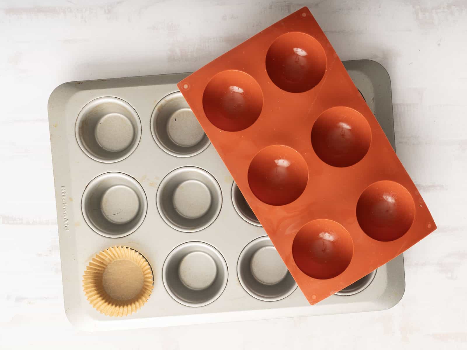 Muffin tin with a silicone mold on top, featuring one paper liner in a cup, perfect for baking delicious quiche muffins on a light surface.