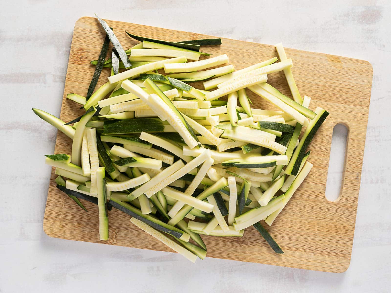 Sliced zucchini sticks, lightly dusted with Pecorino, are piled on a wooden cutting board.