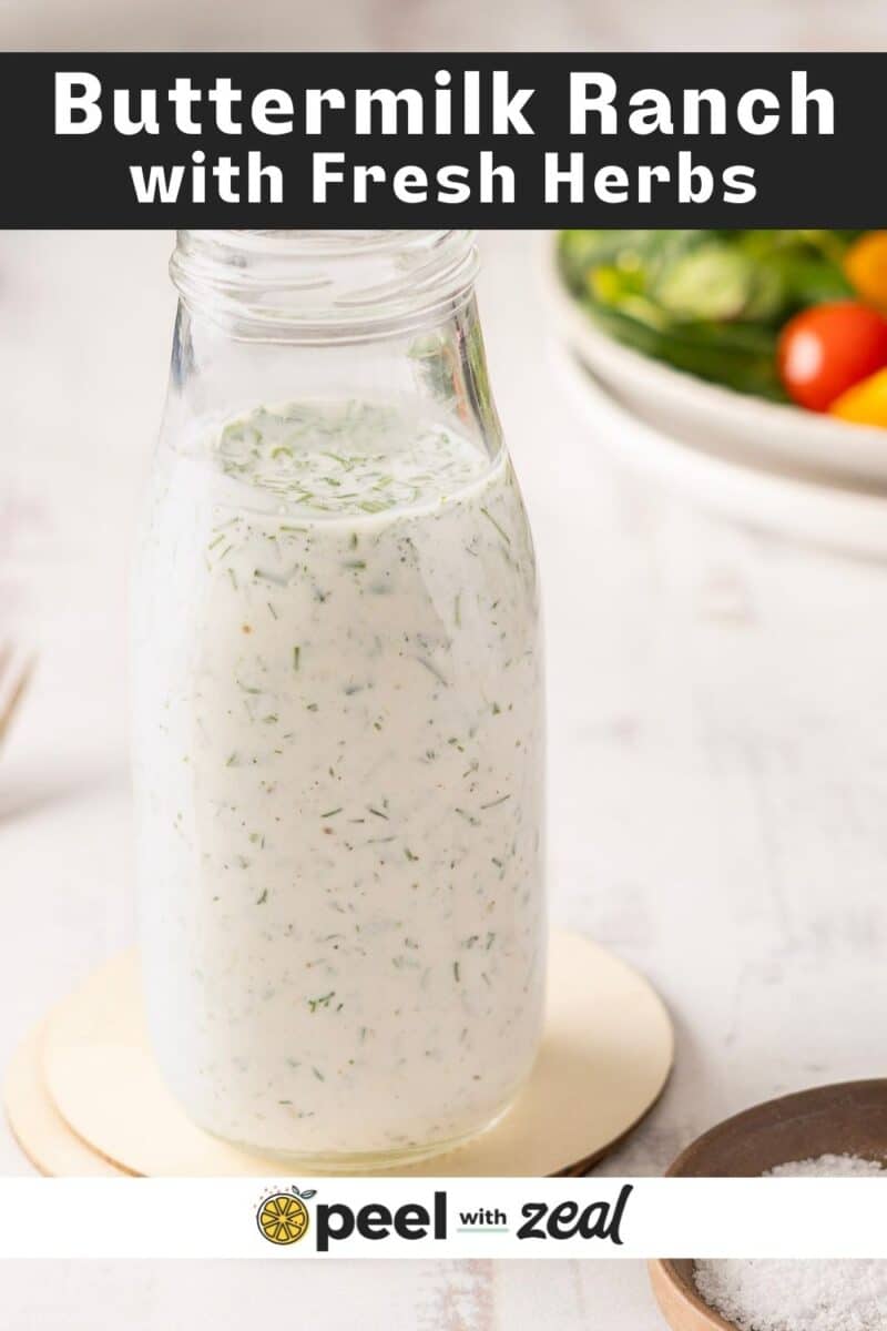 A bottle of creamy buttermilk ranch with herbs stands beside a bowl of fresh tomatoes.