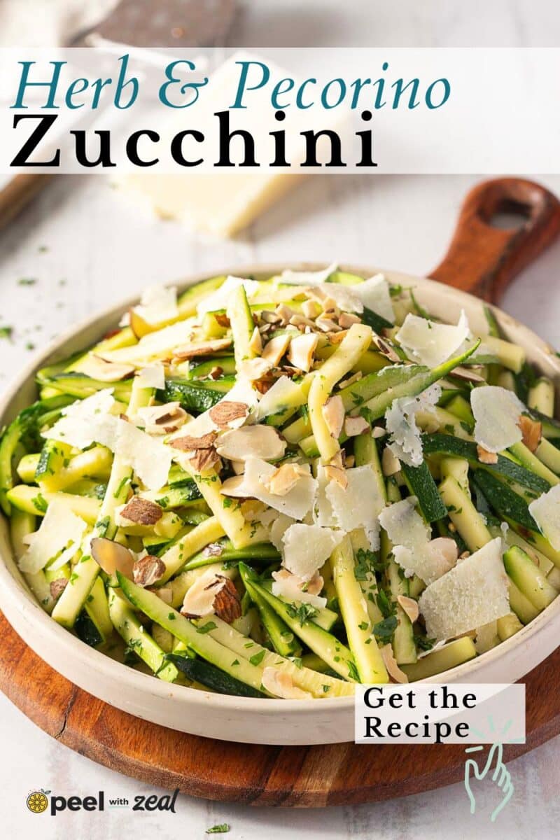 A bowl of zucchini ribbons, freshly sautéed for added flavor, is topped with sliced almonds and cheese shavings on a wooden serving board. Text reads, "Herb & Pecorino Zucchini. Get the Recipe.