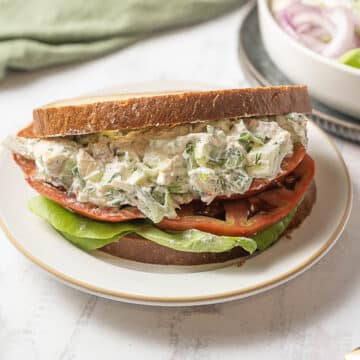 A sandwich with chicken salad, lettuce, tomato, and toasted bread is served on a white plate.