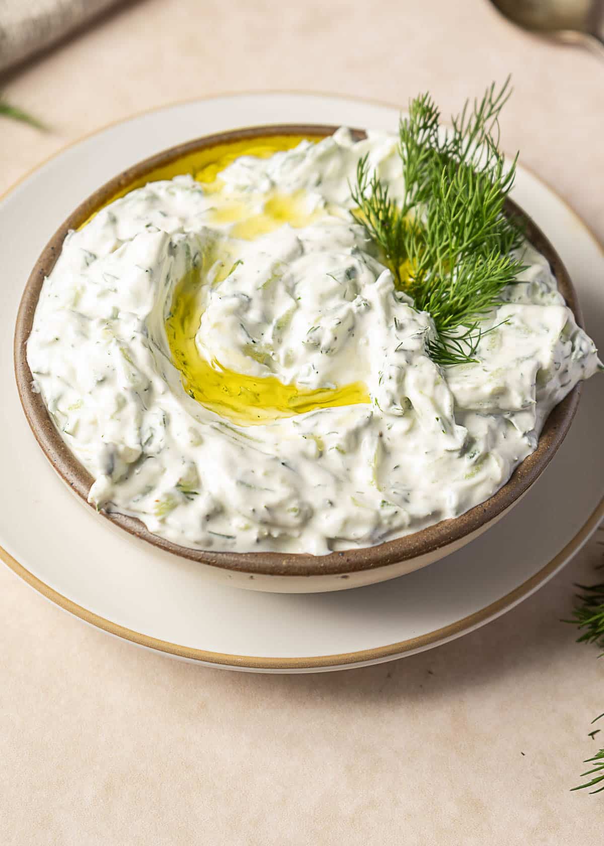 A bowl of creamy herbed dip garnished with fresh dill and a drizzle of olive oil, placed on a white plate.