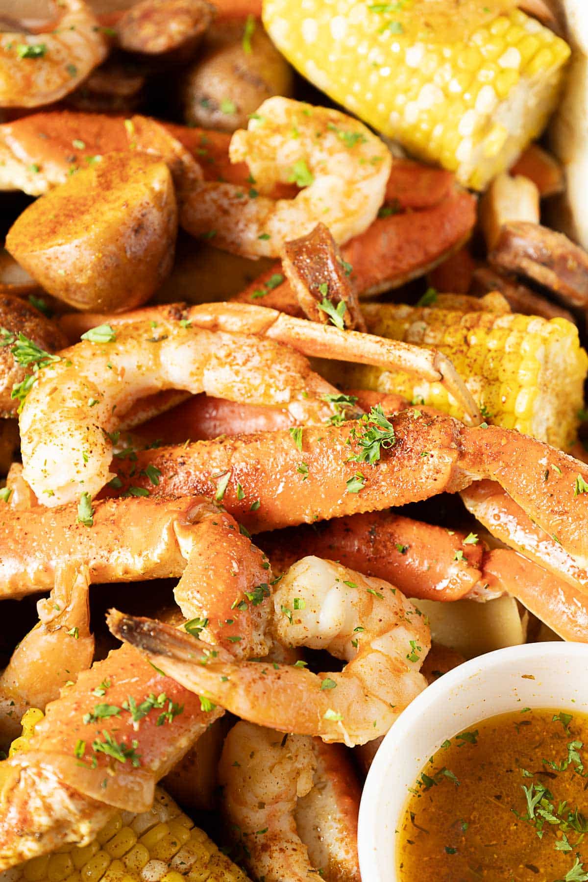 A close-up of a seafood boil with crab legs, shrimp, corn on the cob, potatoes, sausage, and a cup of melted butter, garnished with herbs.